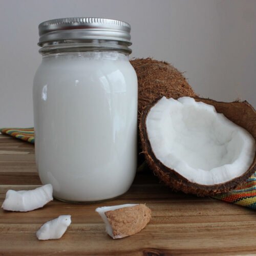 Glass jar of homemade coconut milk standing next to a split open coconut