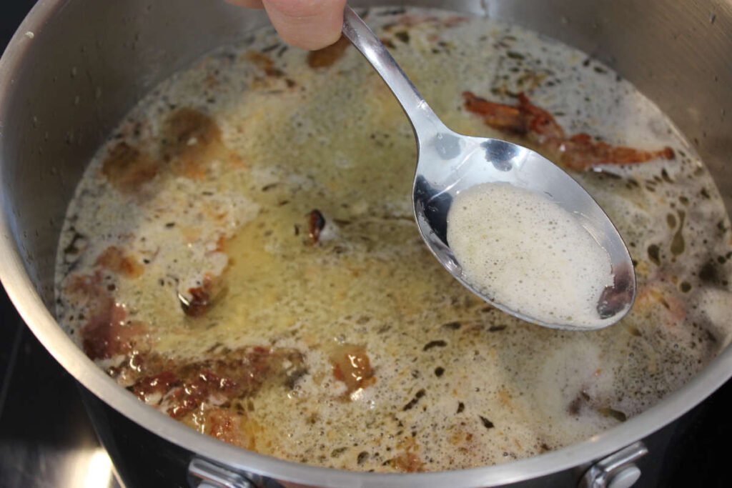 Close-up of a spoon skimming foam and impurities from the surface of simmering homemade chicken stock in a large pot.