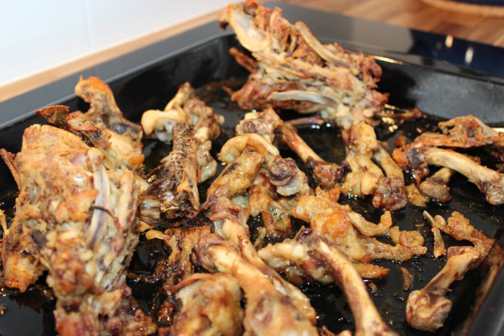 Roasted chicken bones and scraps on a baking tray, ready to be used for making homemade chicken stock.