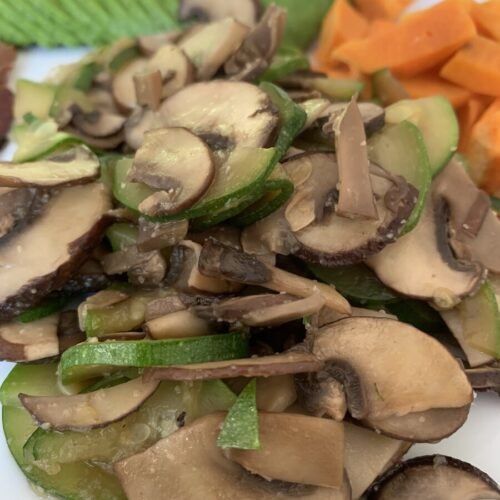 a white plate with an AIP breakfast, which consists of some fresh avocado, microwaved sweet potato and the star of the dish the sautéed mushrooms and zucchini. An easy AIP breakfast