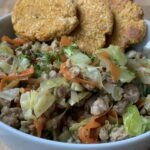 Bowl containing a portion of asian-inspired pork with cabbage and carrot. Served with sweet potato patties