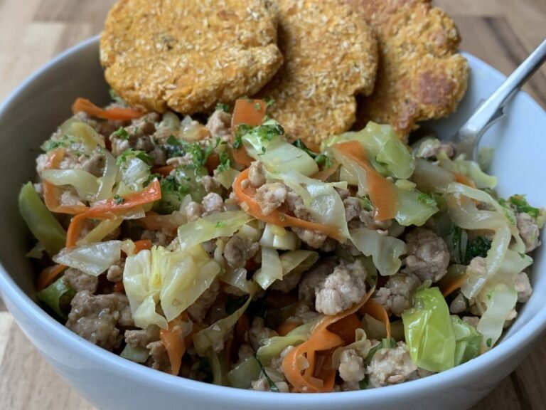 Bowl containing a portion of asian-inspired pork with cabbage and carrot. Served with sweet potato patties