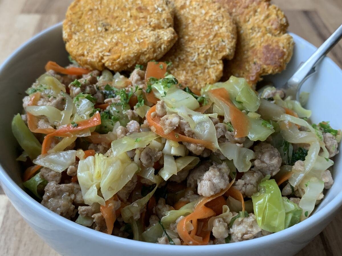 Bowl containing a portion of asian-inspired pork with cabbage and carrot. Served with sweet potato patties