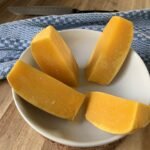 A white bowl with quarters of butternut on a wooden counter with a blue dishtowl in the background.