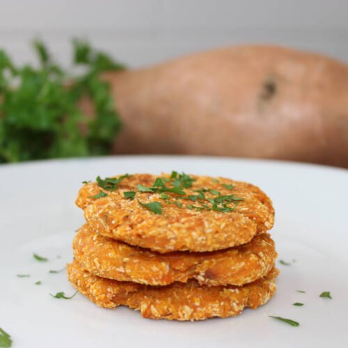 Gluten-free sweet potato cakes stacked on a plate, with fresh herbs and whole sweet potato for decoration