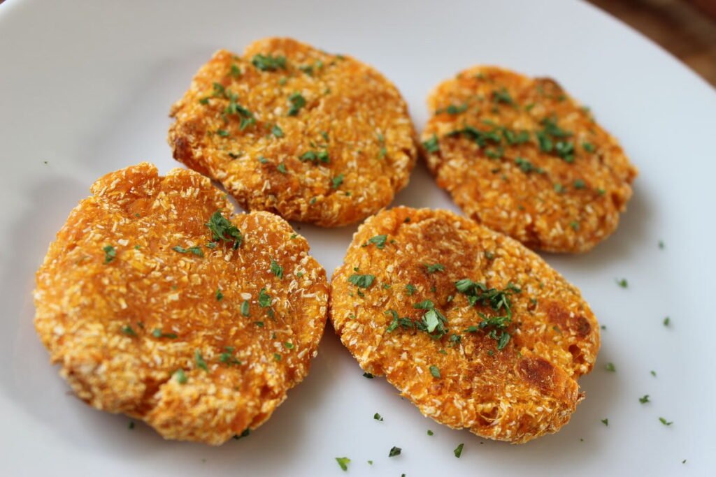Four sweet potato patties on a white plate garnished with finely chopped parsley