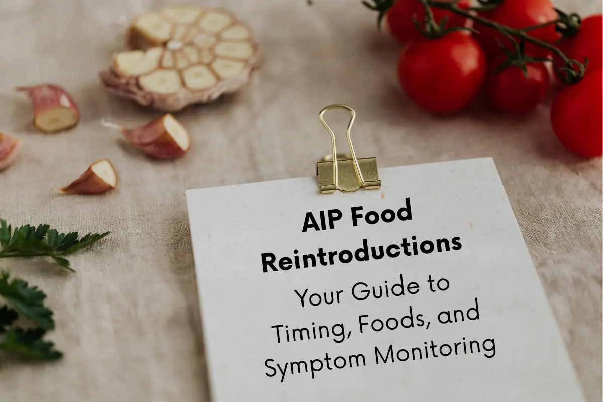 Clipboard lying next to some cut up garlic and tomatoes. Text on the clipboard reads: AIP Food Reintroductions: Your guide to timing, foods and symptom monitoring