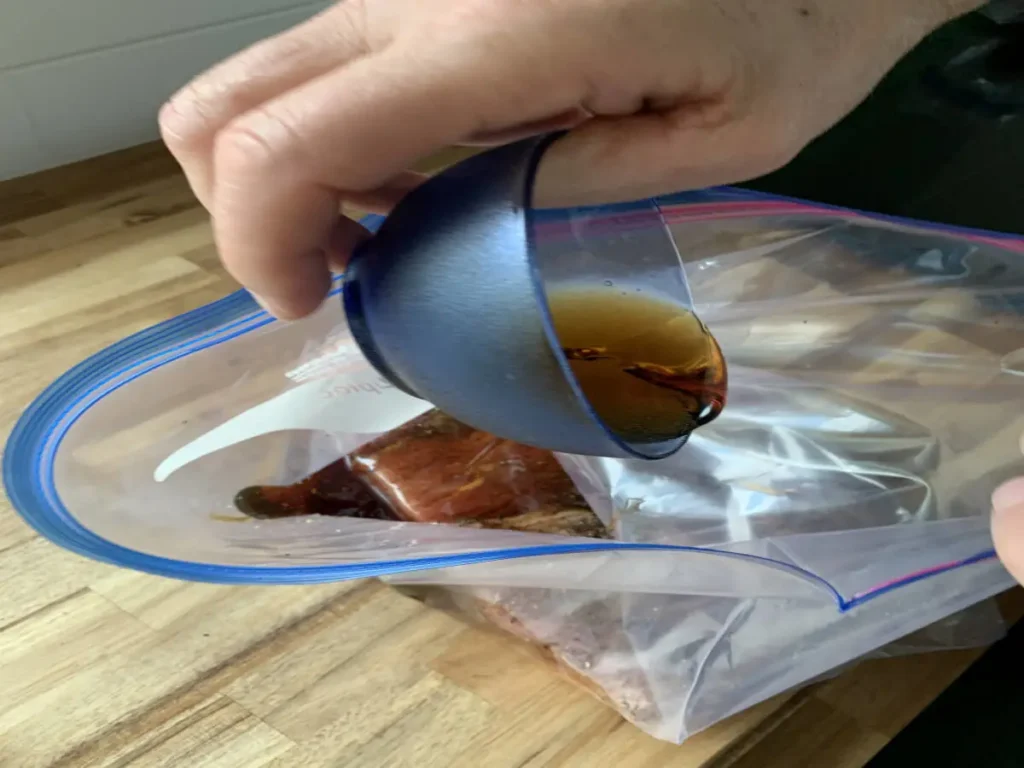 Pouring maple syrup onto the seasoned pork belly as part of the curing process for AIP bacon.