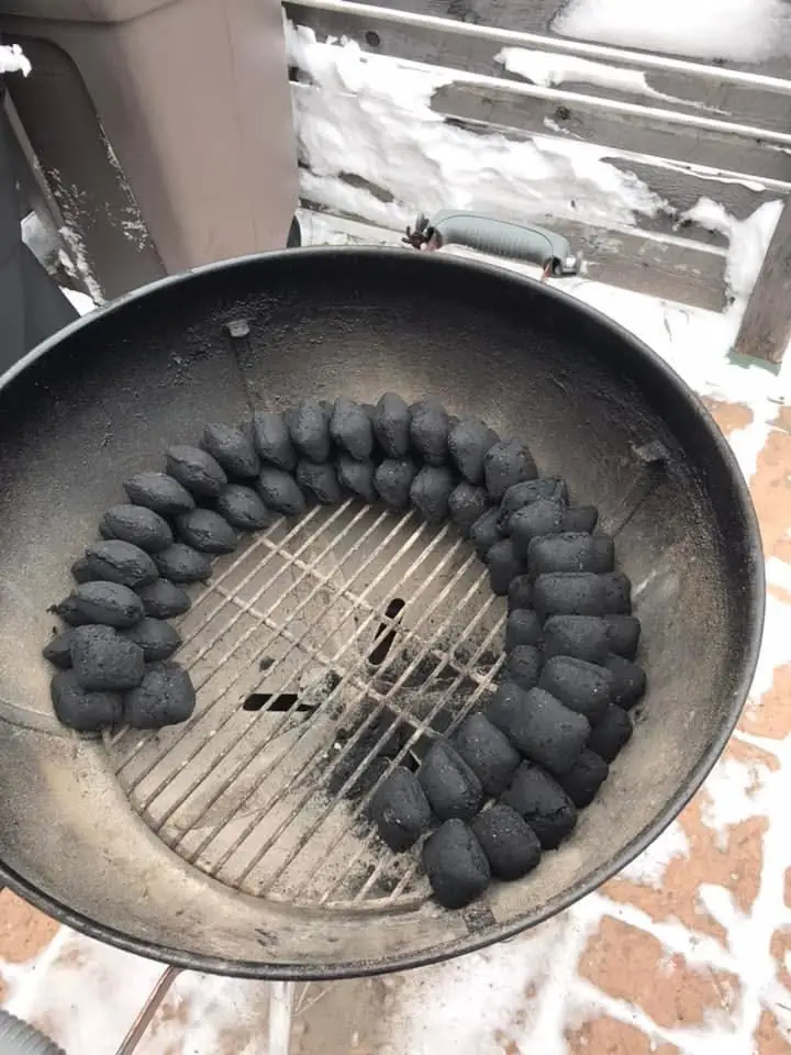 A kettle BBQ with a complete BBQ snake before adding wood chips, lit coal and a water pan. The snake runs around the perimeter of the kettle with two roas of briquettes at the bottom and a single row on top.