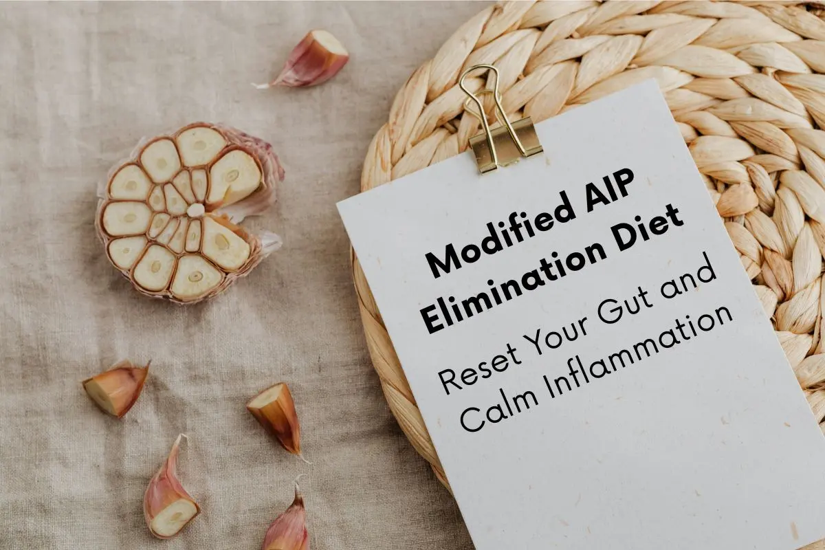 Clipboard lying next to some cut up garlic. Text on the clipboard reads: Modified AIP Elimination Diet: Reset your gut and calm inflammation.