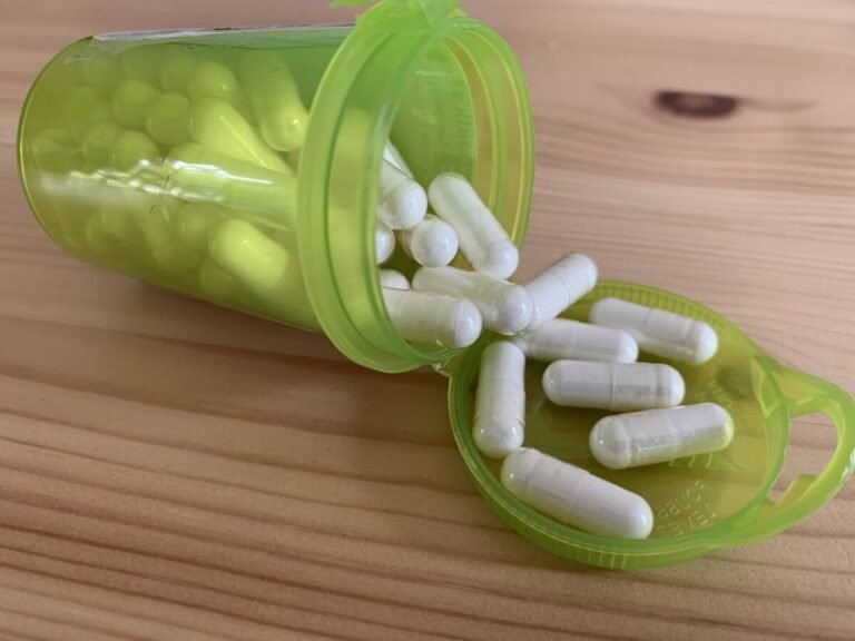 Yellow pill container filled with levothyroxine capsules ling on its side with some pills in the lid of the container.