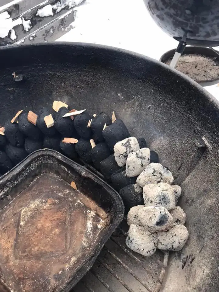 Close up of a BBQ snake showing the water pan in the middle and the charcoal running around the edge of the kettle. The lit coal is added to the start of the snake to start the fuse. Wood chips are added to the start of the snake.