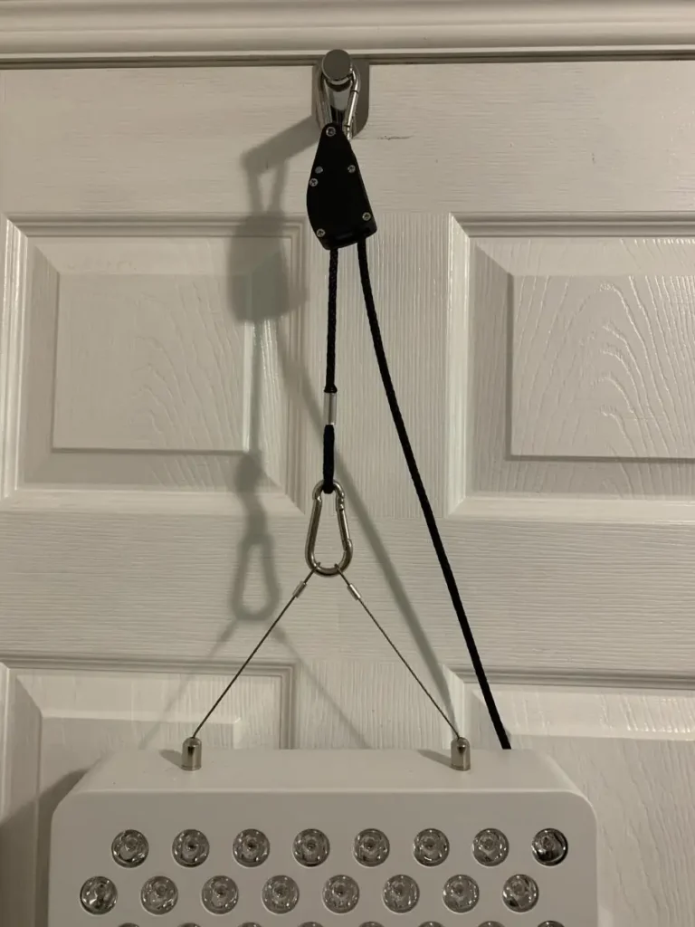 Red light therapy panel hanging on a door with pulley system for height adjustment.
