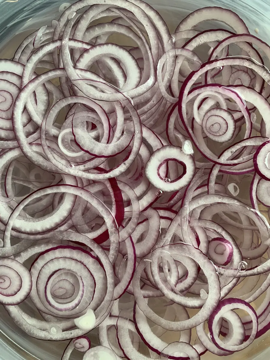 Slicing red onions with a sharp kitchen knife on a wooden cutting board.