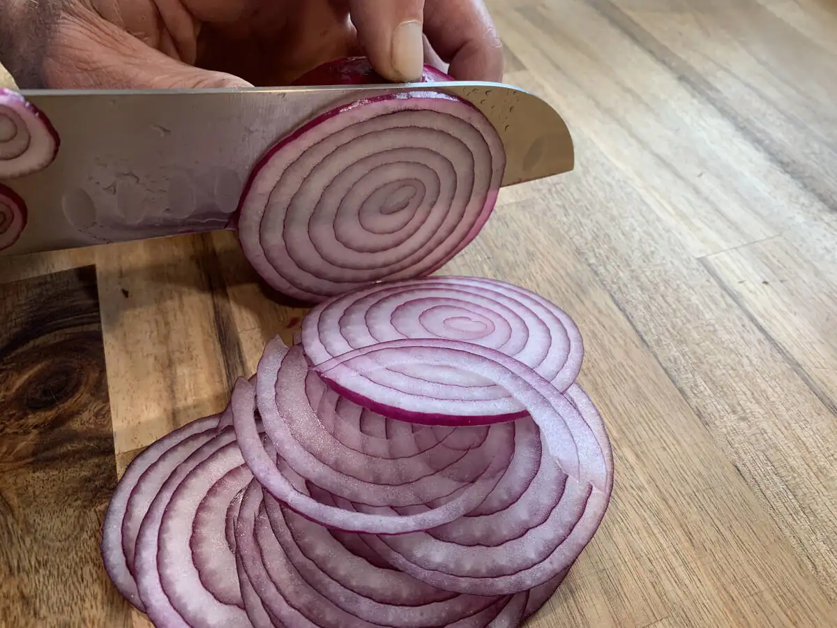 Slicing red onions with a sharp kitchen knife on a wooden cutting board.
