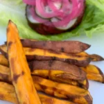 Golden delicious sweet potato fries with an AIP compliant burger in the background.
