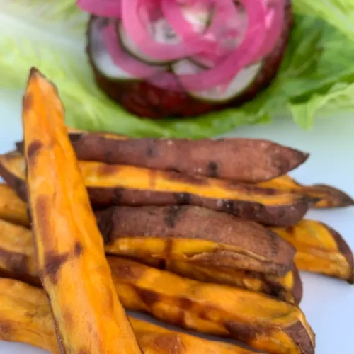 Golden delicious sweet potato fries with an AIP compliant burger in the background.