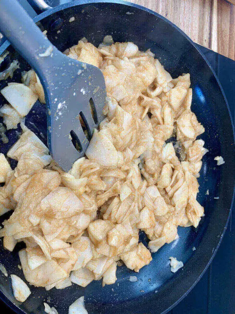 Apple pie filling an a frying pan being stirred by a spatula.