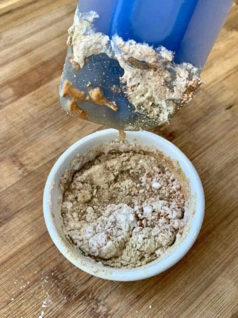 Small bowl containing all the spices and maple syrup and lemon juice for the apple pie filling, with a blue spatula mixing the ingredients together.