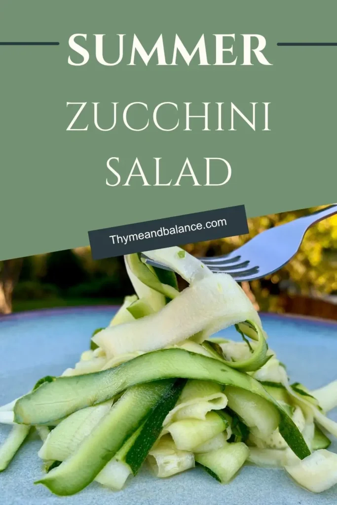 A fork lifting a ribbon of zucchini from a plate of fresh zucchini salad with outdoor background.