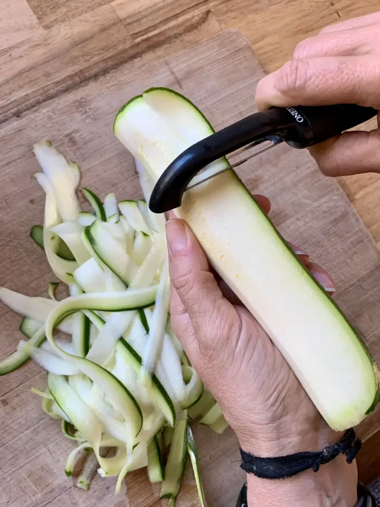 Using a vegetable peeler to peel zucchini ribbons for the courgette salad