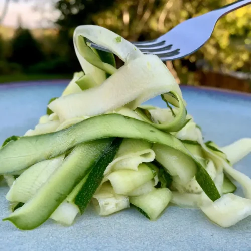 Fork lifting tender zucchini ribbons on a plate, served as a light vegetable side dish.