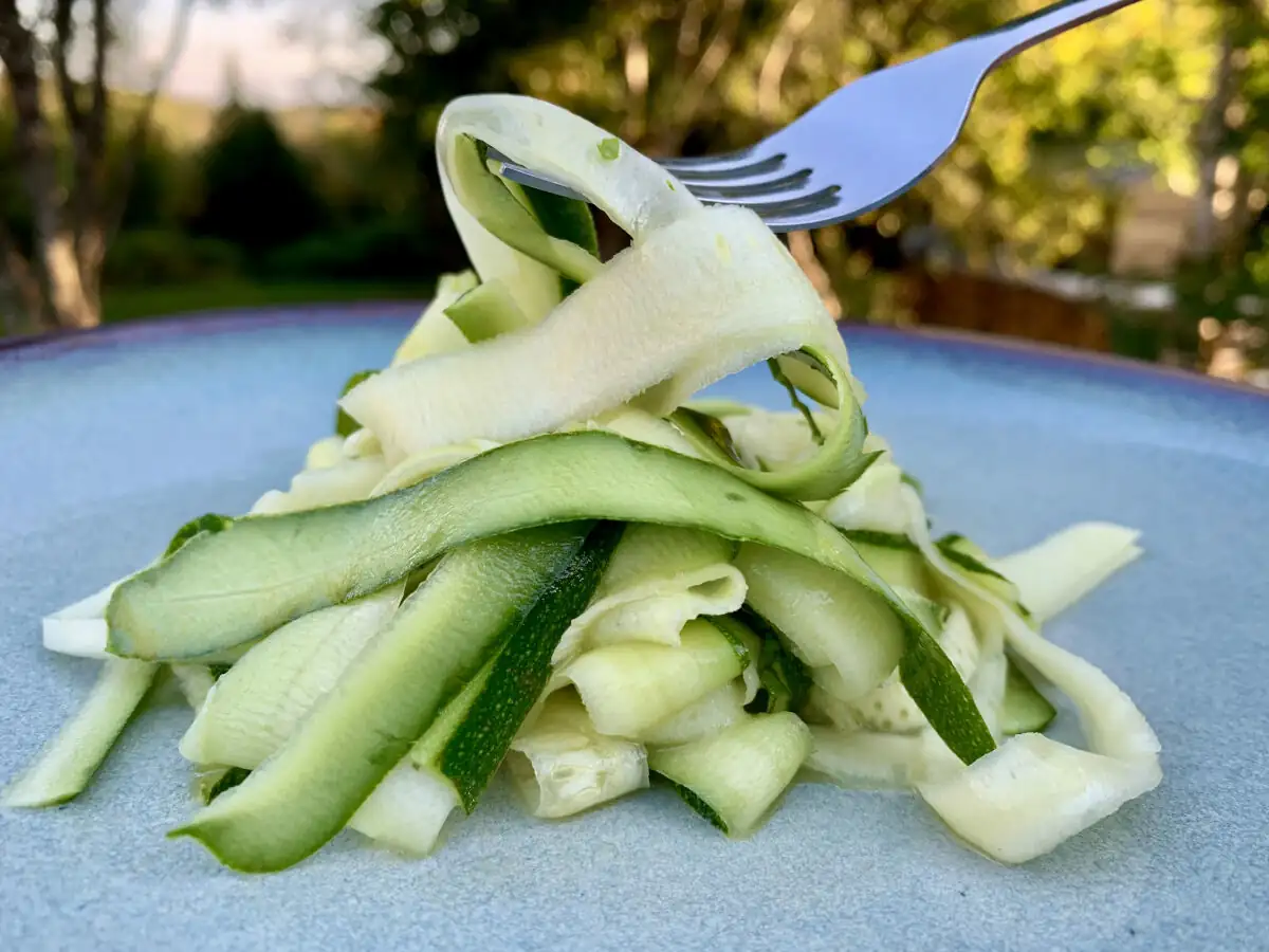 Fork lifting tender zucchini ribbons on a plate, served as a light vegetable side dish.