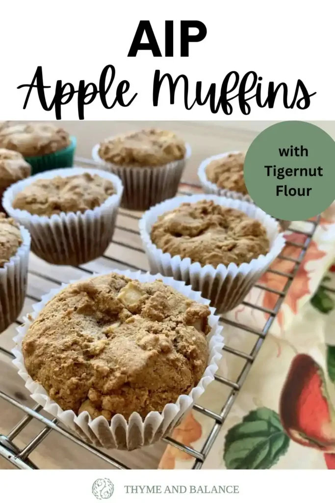 Muffins lying on a cooling rack on a wooden counter with a dish towel. Text overlay reads: AIP Apple muffins with tigernut flour