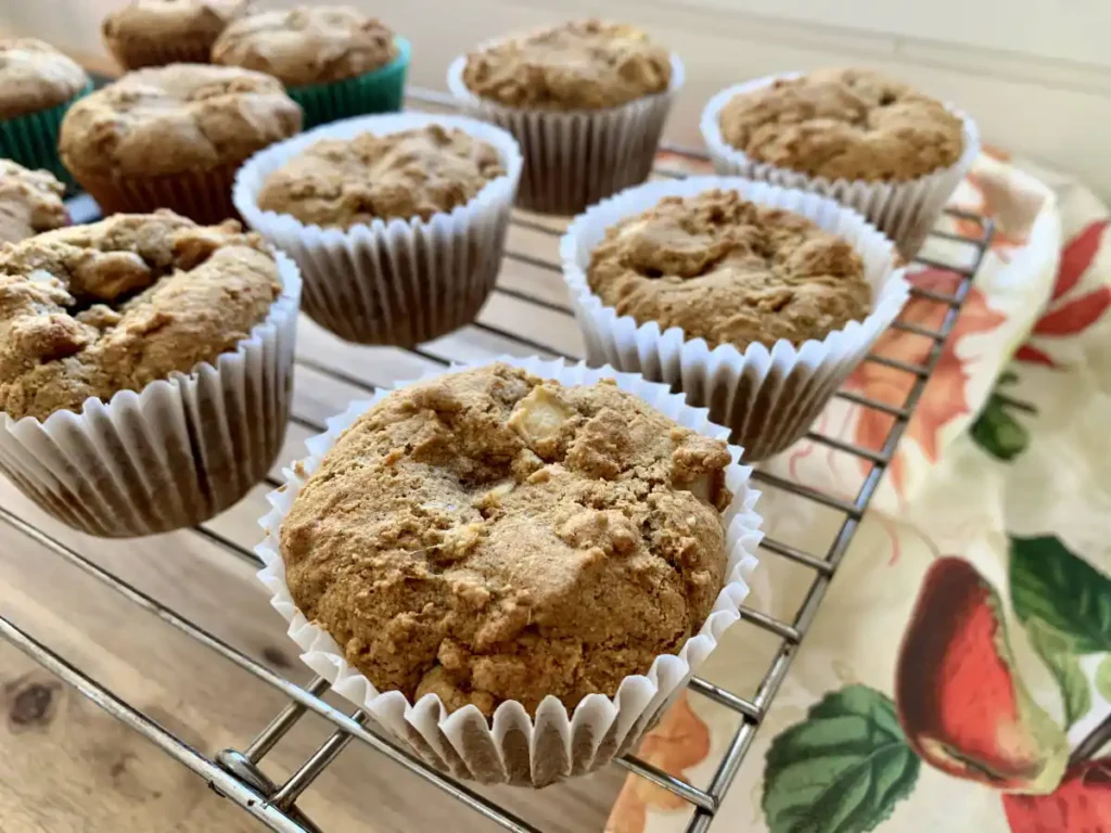 AIP muffins sitting on a cooling rack on top of a wooden counter and a fall coloured dishtowel underneath.