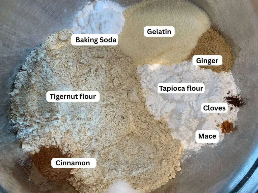 Bowl with dry ingredients for AIP apple ,uffins. Labels read tapioca flour, tigernut flpour, baking soda, cinnamon, gelatin, ginger, mace and cloves