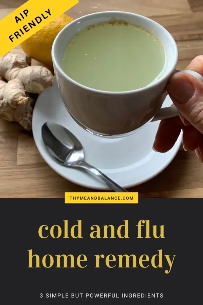 Image of a hand holding a white cup with a lemon, ginger and honey drink next to a fresh ginger and lemon. Text overlay reads AIP friendly. Cold and flu home remedy. 3 simple but powerful ingredients by thymeandbalance.com