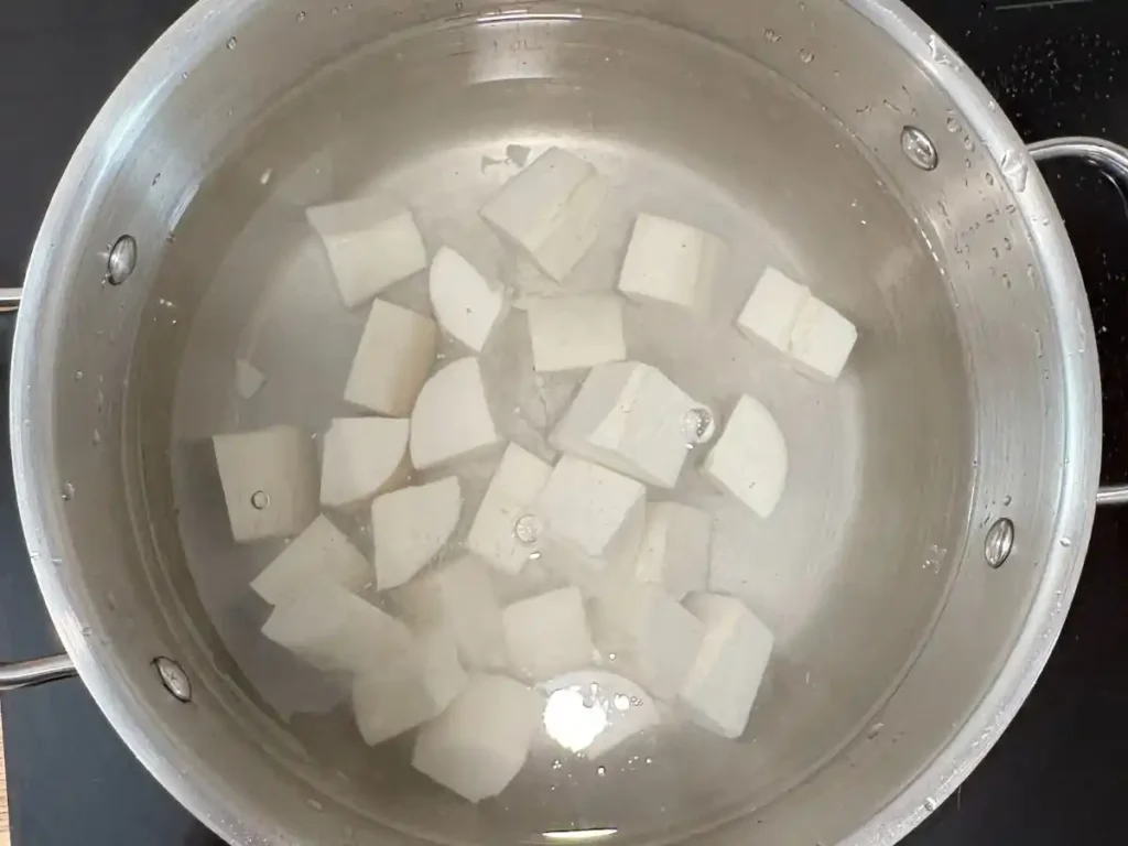 pot on cooktop filled with water and peeled and diced cassava