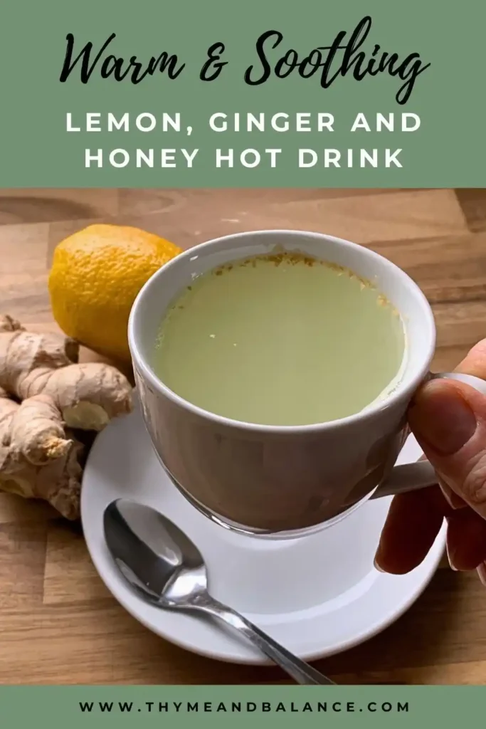 Image of a hand holding a white cup with a lemon, ginger and honey drink next to a fresh ginger and lemon. Text overlay reads warm and soothing lemon, ginger and honey hot drink by thymeandbalance.com