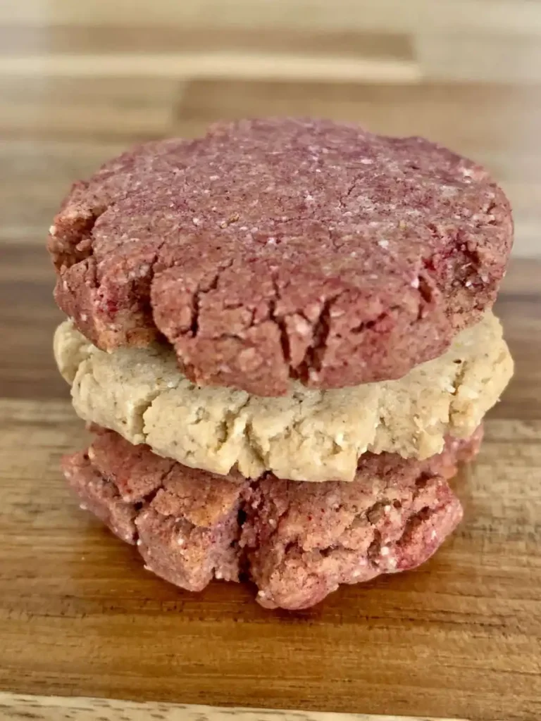 three cookies stacked on top of each other on a wwoden counter. THe middle cookie is white, the other two are pink