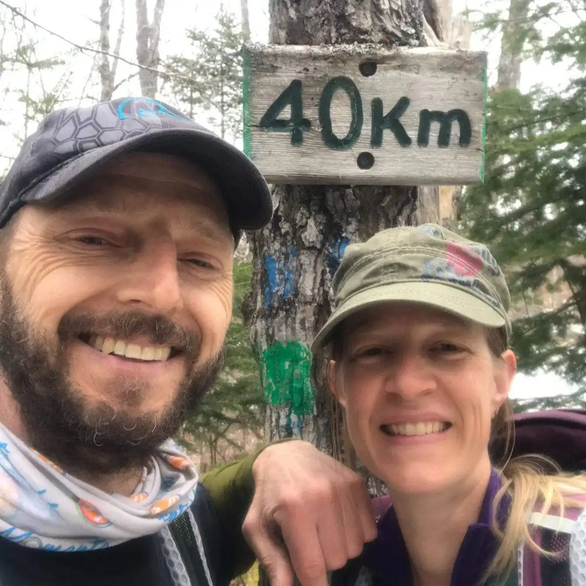 Woman and man wearing caps standing in front of a tree with a sign on it which says "40km"