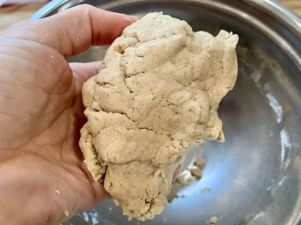hand holding cookie dough over a silver mixing bowl